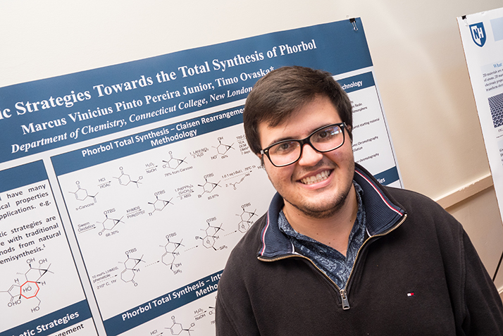 A student smiles in front of a poster describing his science research. 