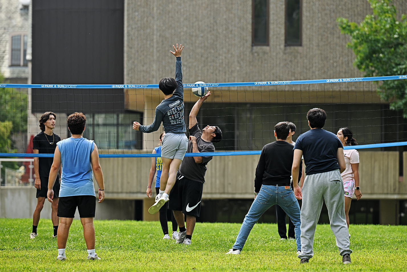 College students play volleyball on a library green.