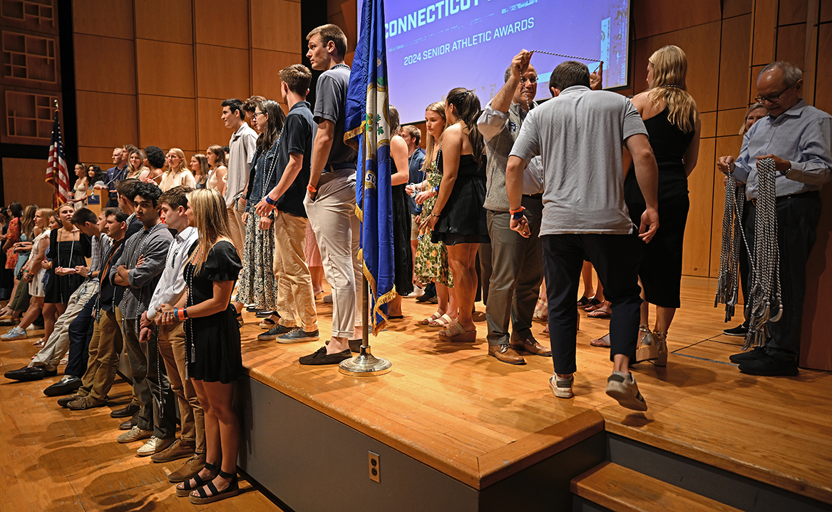 Student athletes gather on a stage to be honored and presented with achievement cords to wear during commencement.