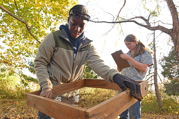 Field archeology student Francis Sesenaya ’24 sifts soil from a test pit as Dennis Delaney ’26 takes measurements during subsurface archaeological investigations on November 12, 2023