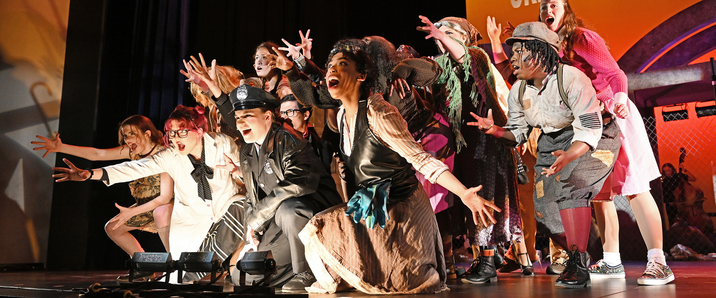 Large group of actors sing finale of opening number at the very edge of the stage.