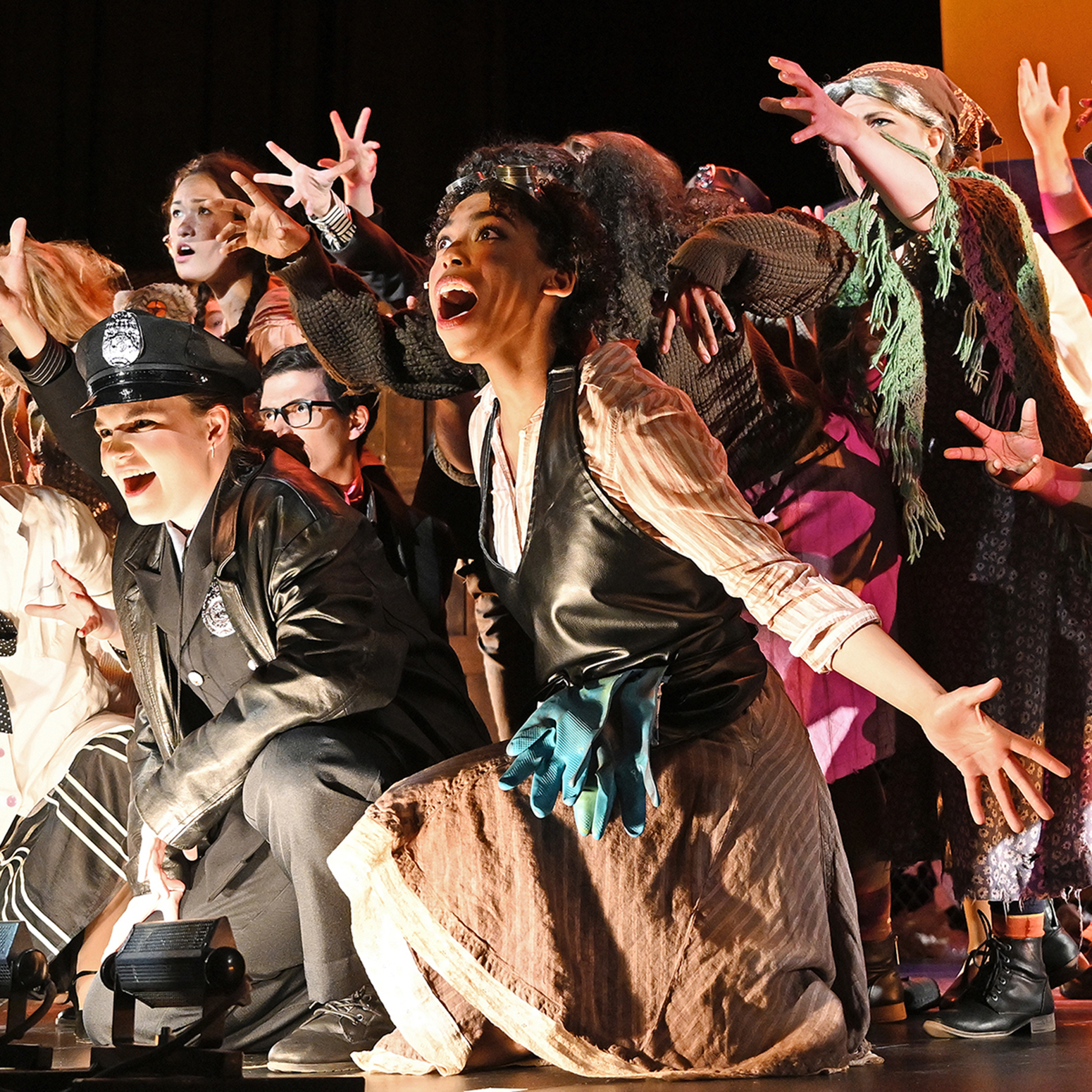 Large group of actors sing finale of opening number at the very edge of the stage.