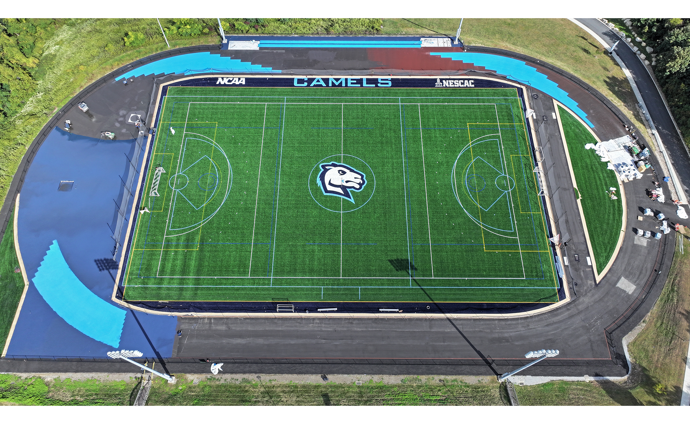 aerial view of turf athletic field and workers laying blue surface to surrounding track.