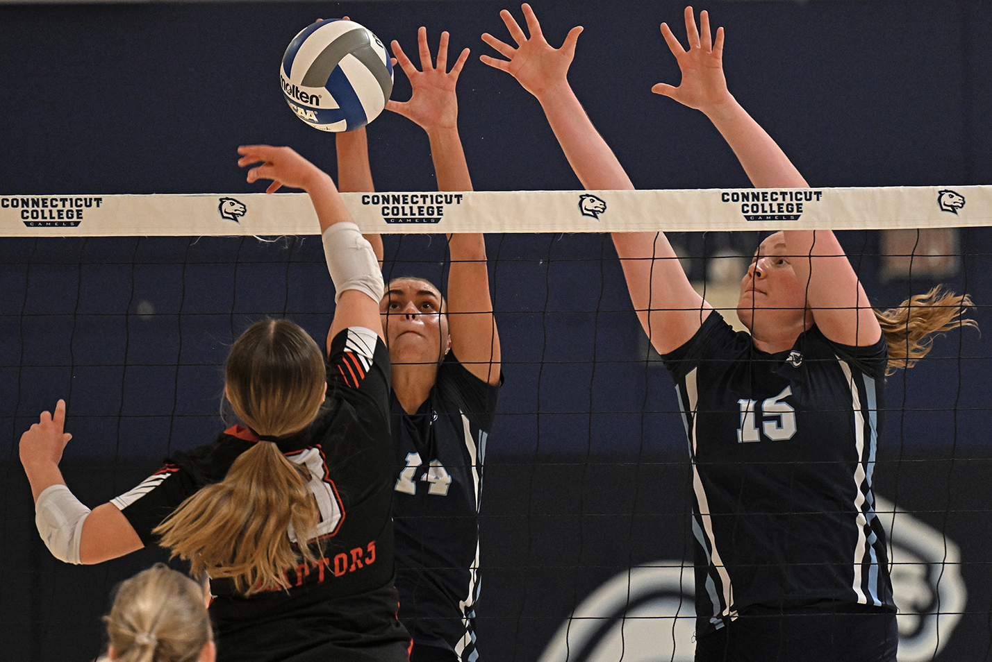 Two volleyball defenders leap to block a shot at the net.