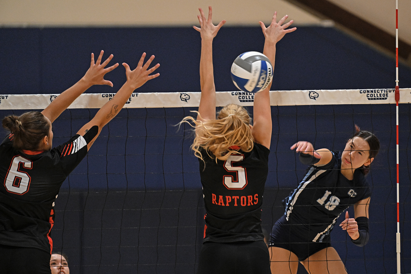 A volleyball player spikes the ball past two defenders.