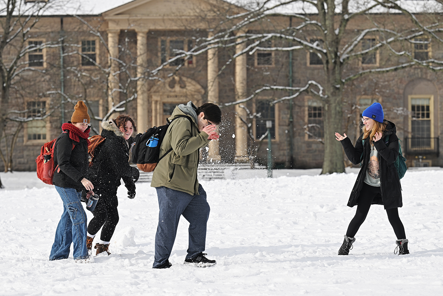 A group of students throw snowballs on a snowy college quad.